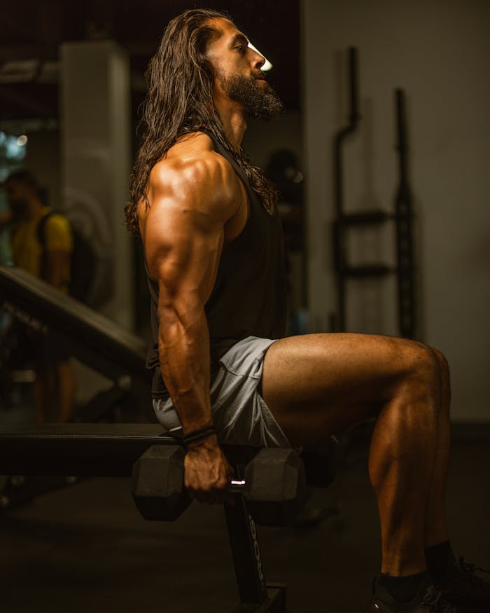 A muscular man works out with dumbbells in a gym, showcasing strength and dedication.
