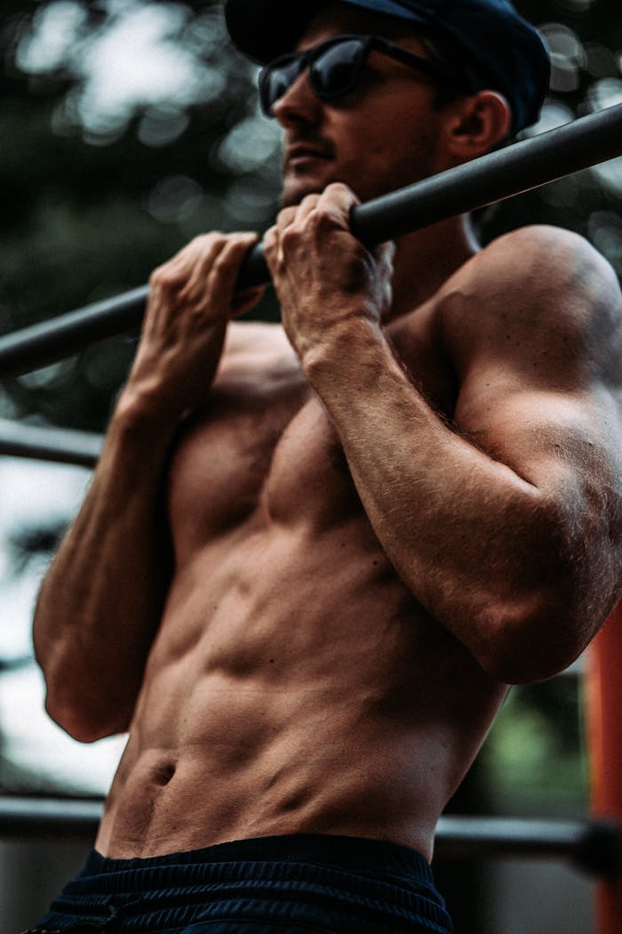 Muscular man performing pull-ups outdoors, showcasing strength and fitness.