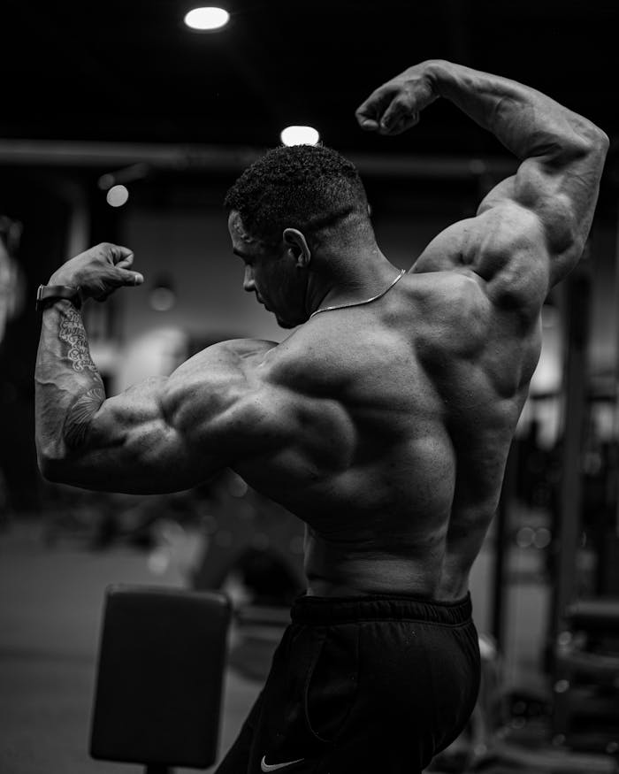 Black and white photo of a bodybuilder flexing muscles indoors.