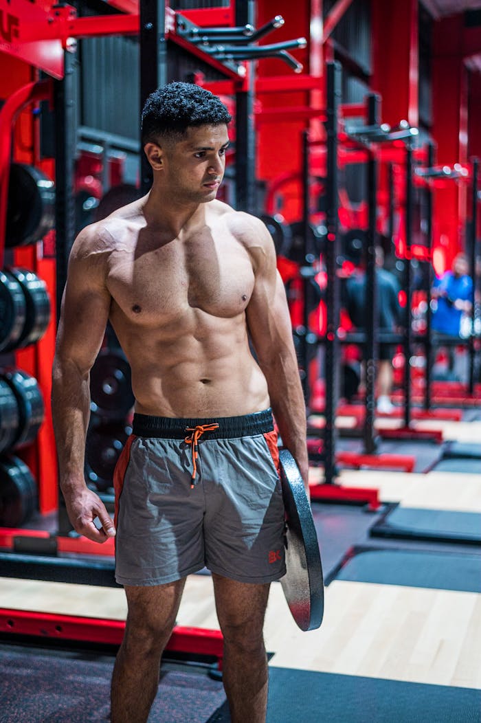 A muscular young man stands confidently in a modern gym holding a weight plate.